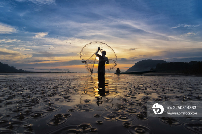 Silhouette of asia traditional fisherman in action when fishing