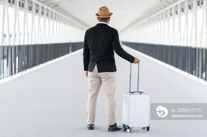 Casual businessman travel with trolley bag walking in the airport terminal. Young man wearing mask a