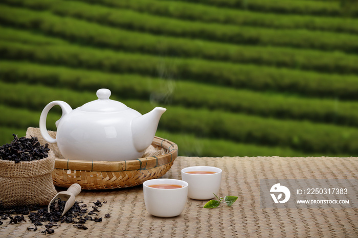 Warm cup of tea with teapot, green tea leaves and dried herbs on the bamboo mat at morning in planta