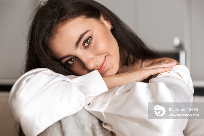 Image of beautiful woman 30s wrapped in blanket smiling, and sitting on couch in apartment