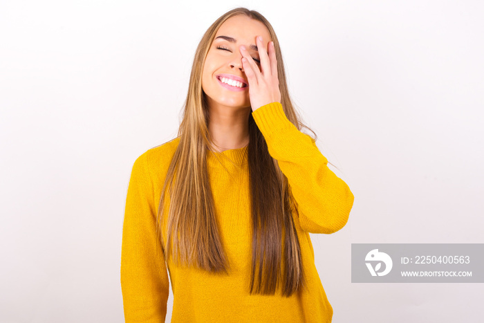 Young caucasian girl wearing yellow sweater over white background makes face palm and smiles broadly