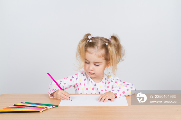 Little girl draws at table pencils.