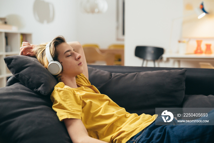 teenage boy relaxing on sofa and listening to a music