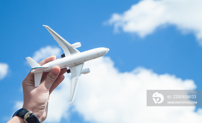 Hand holding airplane model in front of blue sky background. Travel