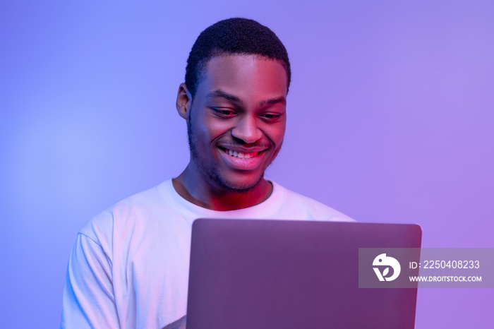 英俊微笑的黑人程序员在霓虹灯下在笔记本电脑上在线工作