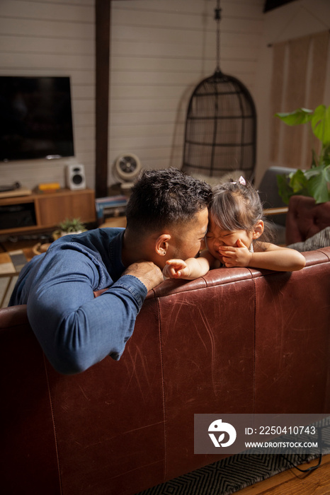 Happy father and daughter playing while relaxing on sofa at home