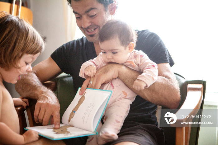 Father reading book with daughters (2-3, 2-5 months)