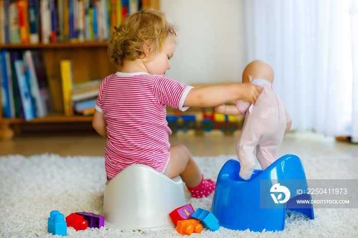 Closeup of cute little 12 months old toddler baby girl child sitting on potty. Kid playing with doll