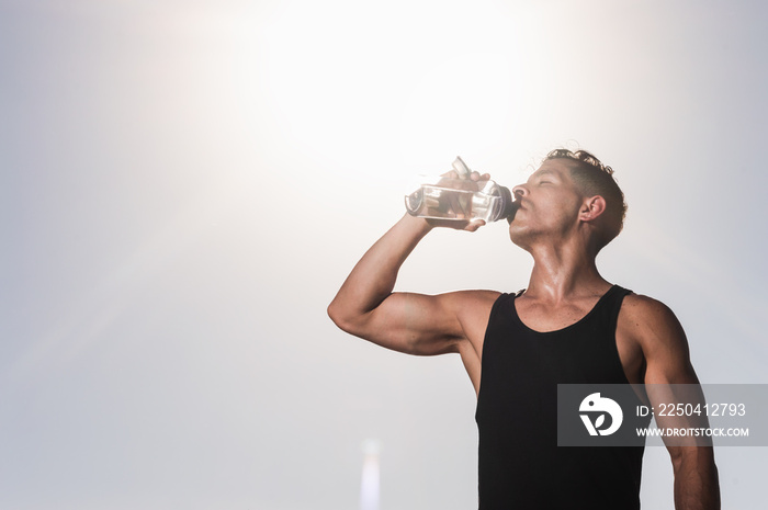 sporty latin young man drinking water during training to avoid dehydration