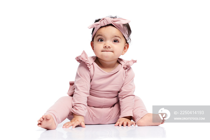 Adorable baby girl in lovely pink outfit and headbandlooking up. Attractive little female kid sittin