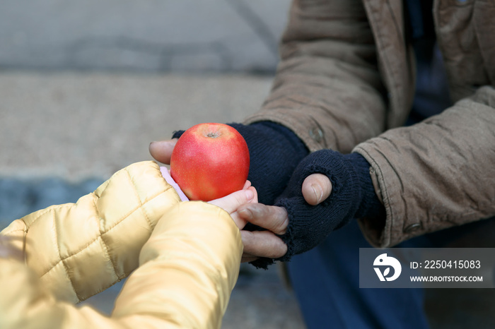 Child gives apple to the beggar.