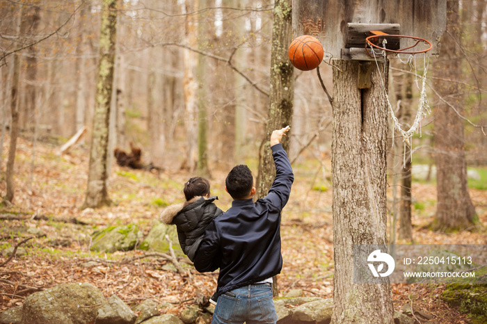 Rear view of father carrying daughter playing basketball while standing in forest