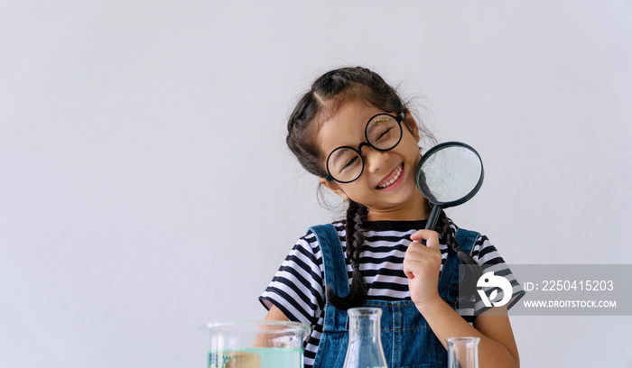 Childhood girl wearing glasses smiling and holding magnifying glass while doing science experiment a