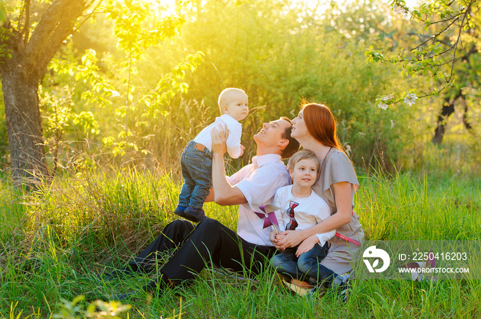 Father, mother and two sons are playing in the garden on sunset