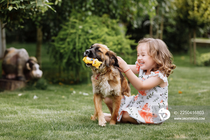 A cute little girl is playing with her pet dog outdooors on grass at home