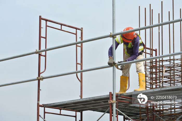 Construction workers wearing safety harness and installing scaffolding at high level in the construc