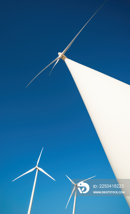 Wind farm with tree power generators against clear blue sky. Vertical shot, dramatic view from below