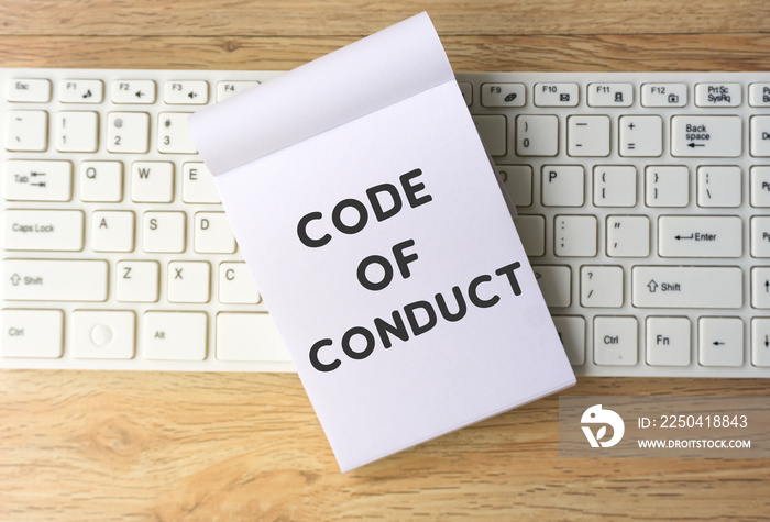 Code of conduct on notepad on top of computer keyboard, wooden table background. Retro style effect.