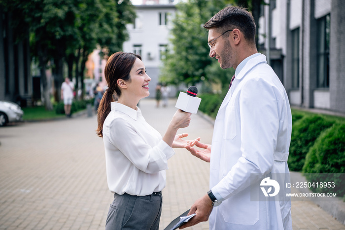 journalist holding microphone and talking with handsome doctor in white coat