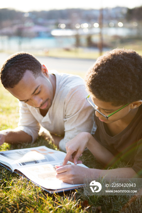 Father and son (10-11) lying on grass and reading book