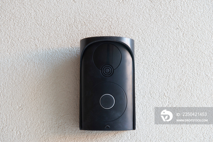 Black intercom without camera on rough beige wall.