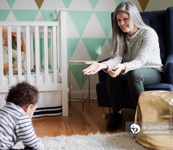 Smiling mother gesturing while looking at son sitting rug in room