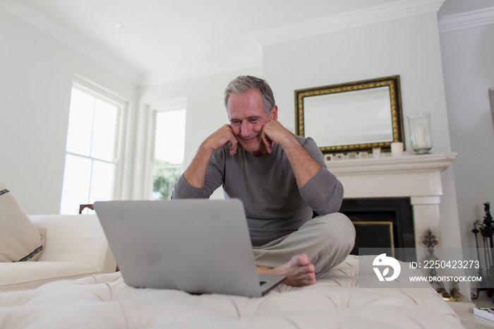 Senior man using laptop on living room ottoman