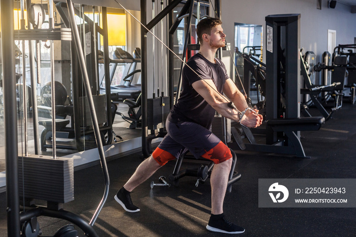 Side view of young adult confident crossfit man standing and doing trx exercises in the gym alone, t