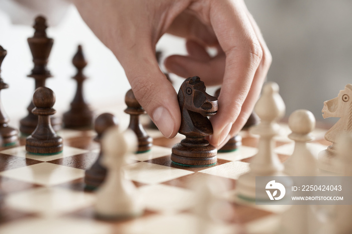 The girl player is holding a horse chess piece in his hand, making a move with a chess piece made of