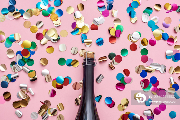 Party started! A bottle of champagne with glittering confetti on pink background.