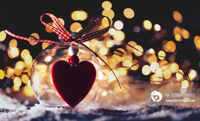 Christmas glass ball with a heart inside on snow.