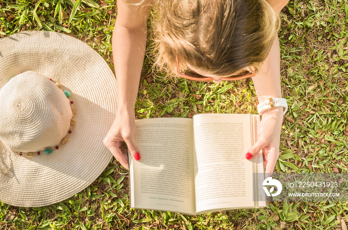 Linda mulher lendo um livro no gramado verde, sol de verão.