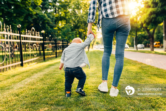 Mom holds the hand of her little child, walks in the park