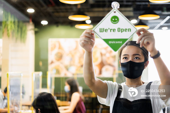 Business owner Asian woman wear protective face mask ppe hanging open sign at her restaurant / café,