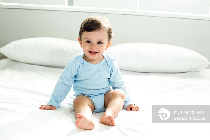 Cute baby boy sitting on bed at home