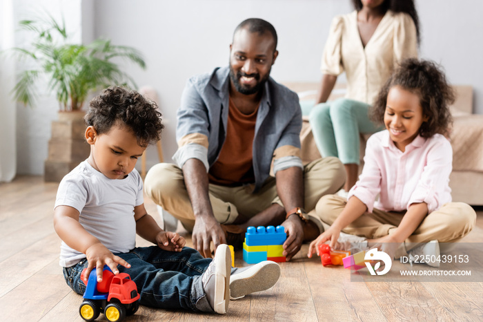 selective focus of african american man and children playing with building blocks on floor near moth