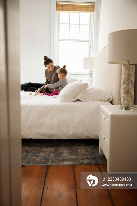 Mother and daughter playing with toys while relaxing on bed at home seen through doorway