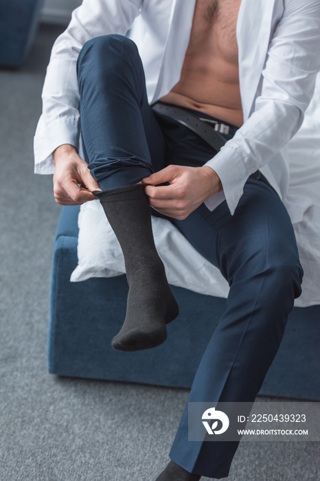 cropped view of man sitting on bed and wearing black socks in bedroom