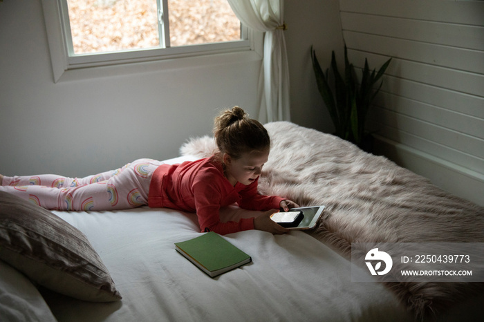 High angle view of girl with tablet computer using mobile phone while lying on bed at home