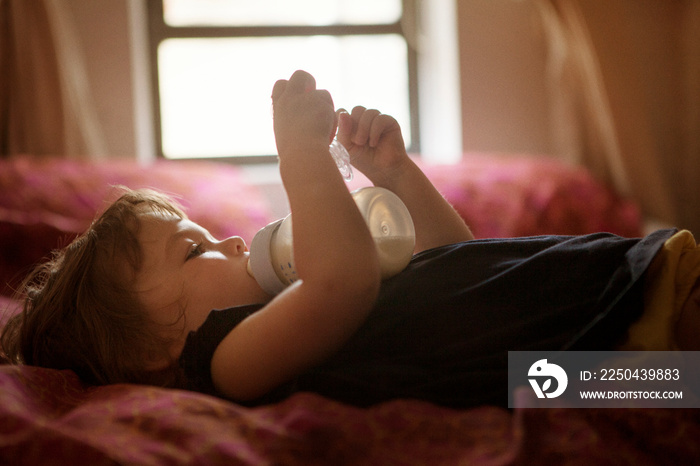 Girl (2-3) lying on bed and drinking milk