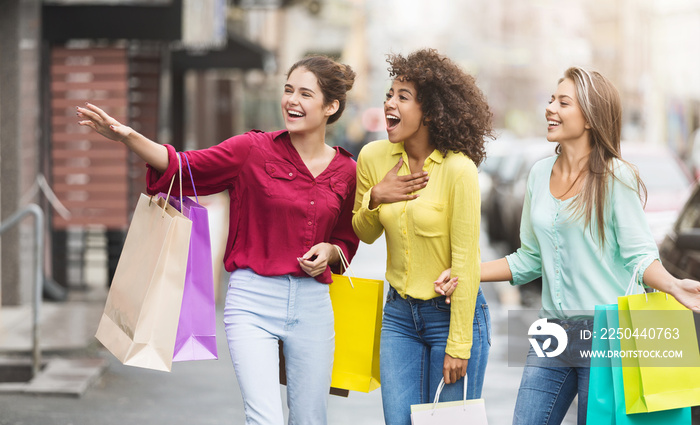 Happy women with shopping bags walking along city street