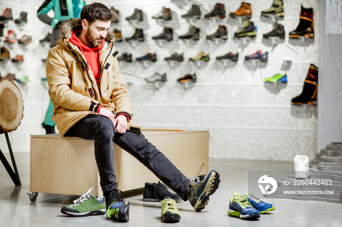 Man in winter jacket trying shoes for mountain hiking sitting in the fitting room of the modern spor