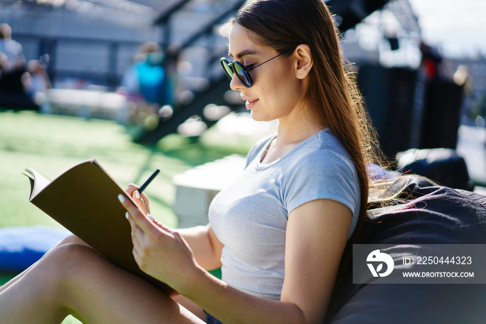 Talented female designer with brunette hair creating sketches during sunny day in campus,millennial 