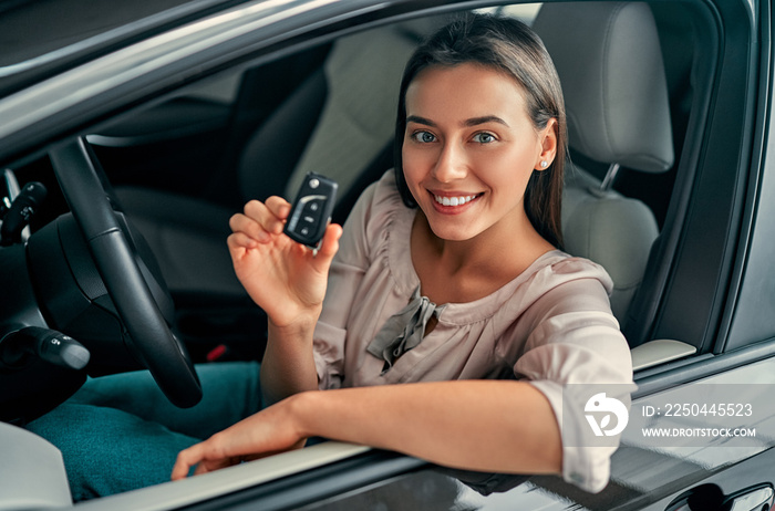 Young happy woman showing the key of new car. Woman buying the car.