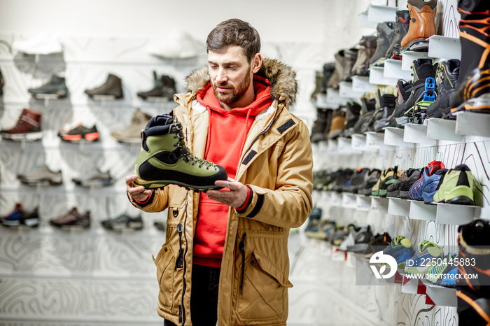 Man in winter jacket choosing trail shoes for mountain hiking in the sports shop