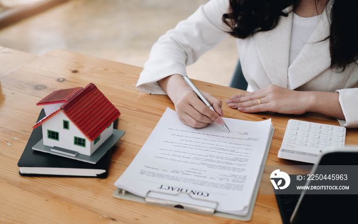 Cropped image of real estate agent assisting client to sign contract paper at desk with house model