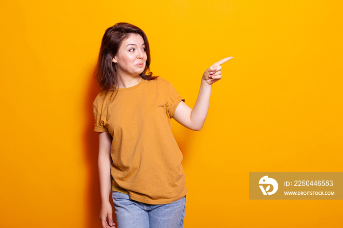 Cheerful woman pointing index finger at right side of studio. Young person pointing aside and standi