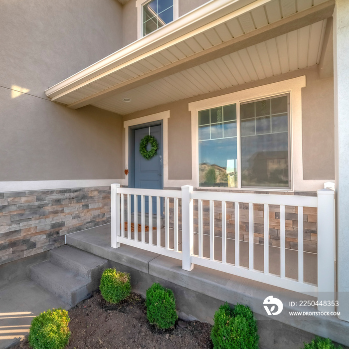 Square Home facade with small porch and blue gray front door with green leafy wreath