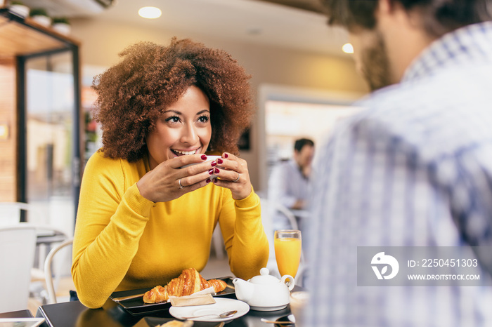 Young trendy couple drinking a coffee and tea at cafe, eating a croissant and feeling happy.