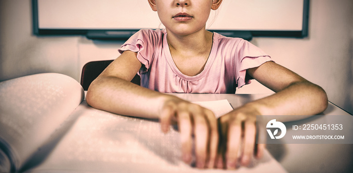 Schoolgirl reading a braille book in classroom